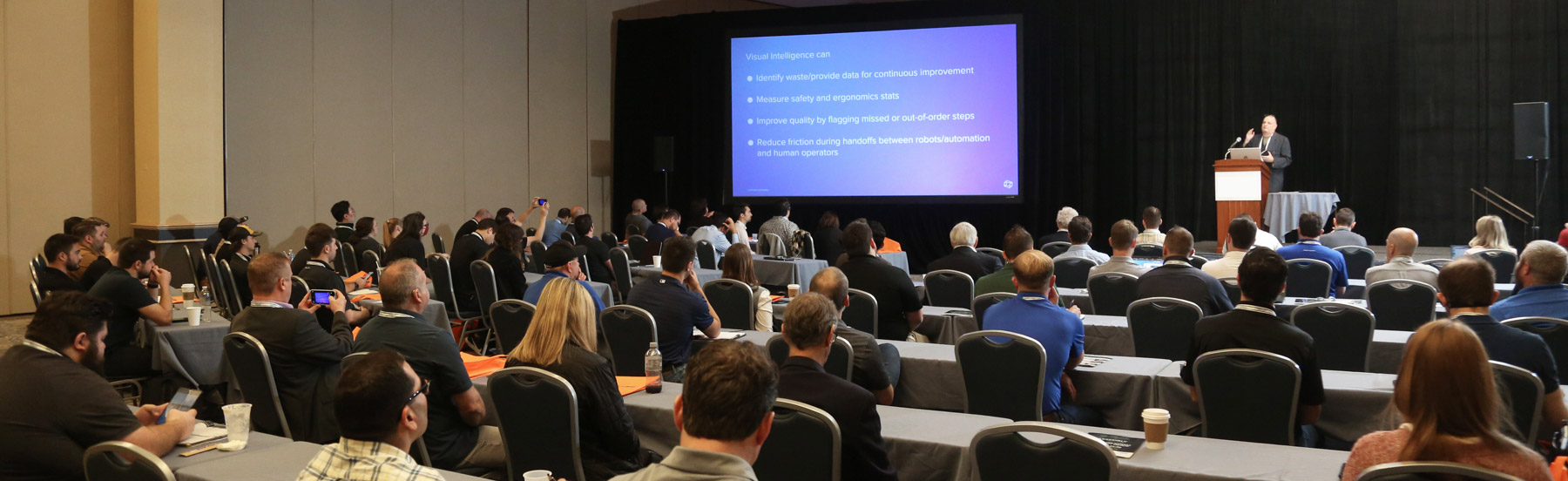 A speaker giving a presentation about visual intelligence to an attentive audience seated at tables in a conference room