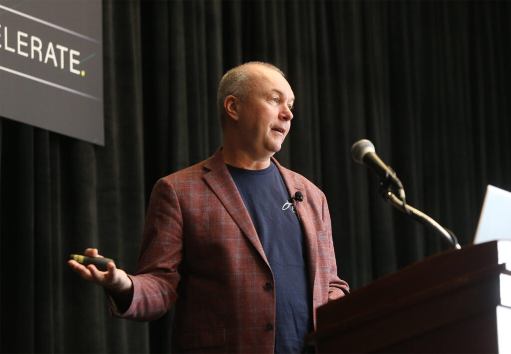 A speaker delivering a presentation from behind a podium, gesturing with one hand